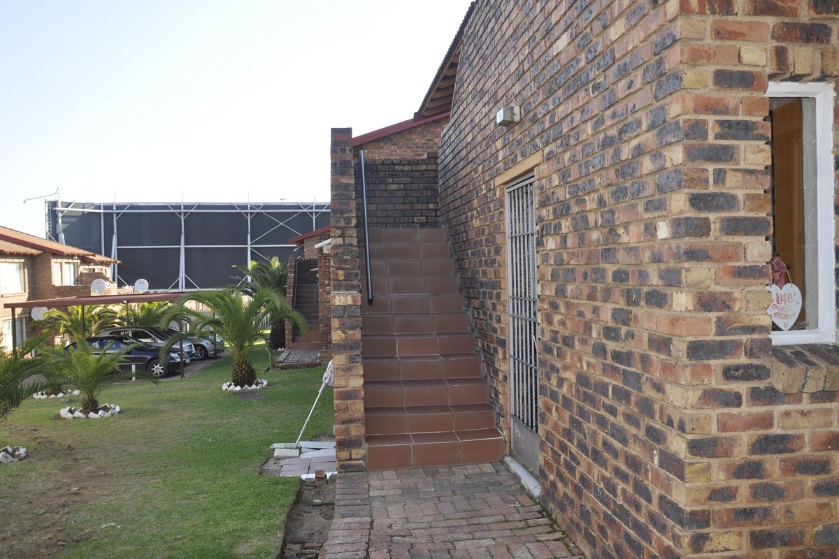 Exterior view of a townhouse featuring a face brick facade, tiled staircase, and paved walkway leading to a secure entrance.