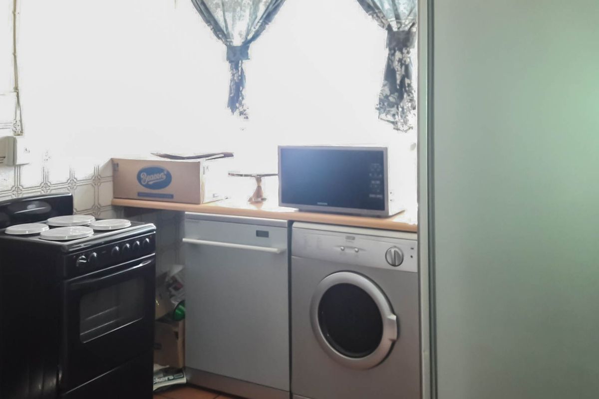 A functional kitchen area featuring a freestanding stove, built-in dishwasher, and washing machine with tiled splashback and laminate countertop.