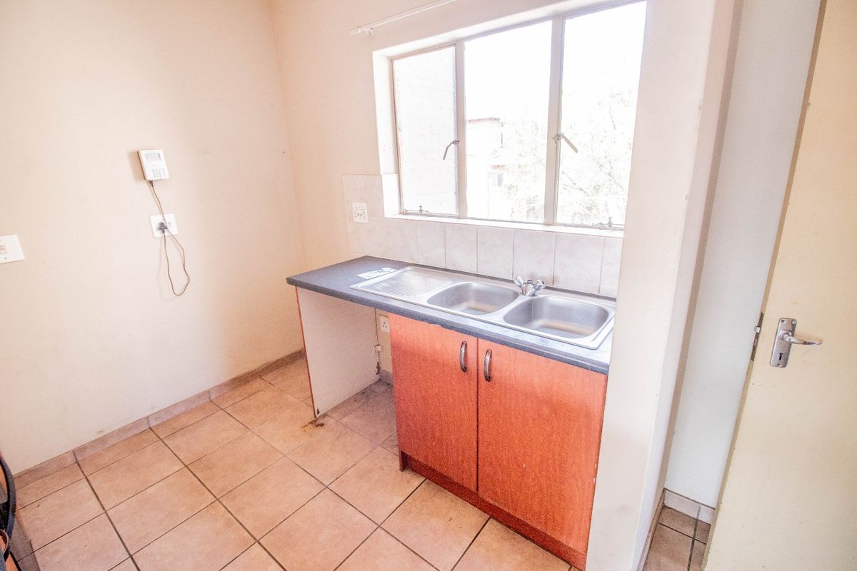 A compact, empty kitchen area featuring a double bowl stainless steel sink, laminate countertop, tiled splashback, and base cabinetry with tiled flooring.