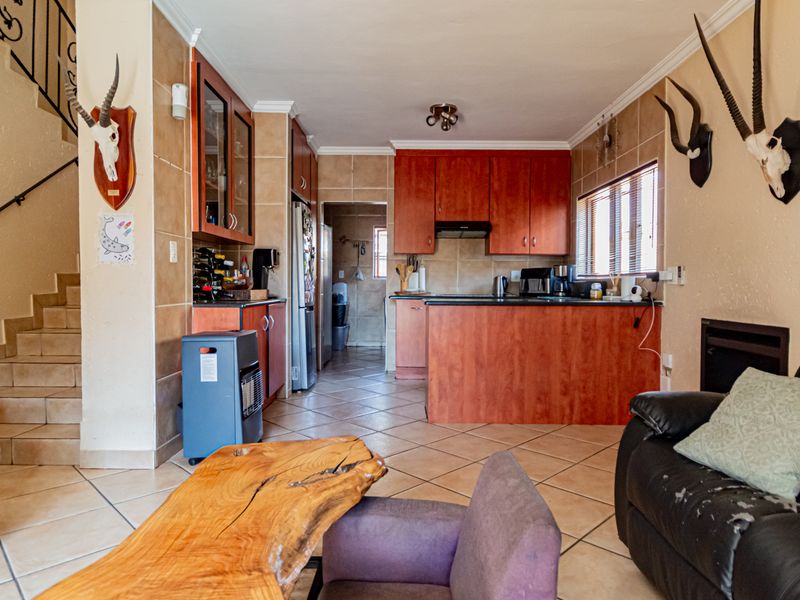 Open-plan living and kitchen area featuring tiled flooring, built-in wooden cabinetry, and an adjacent staircase leading to the upper level.