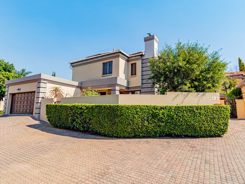 Front exterior view of a townhouse featuring a paved driveway, double garage, and a well-maintained boundary wall with established landscaping.