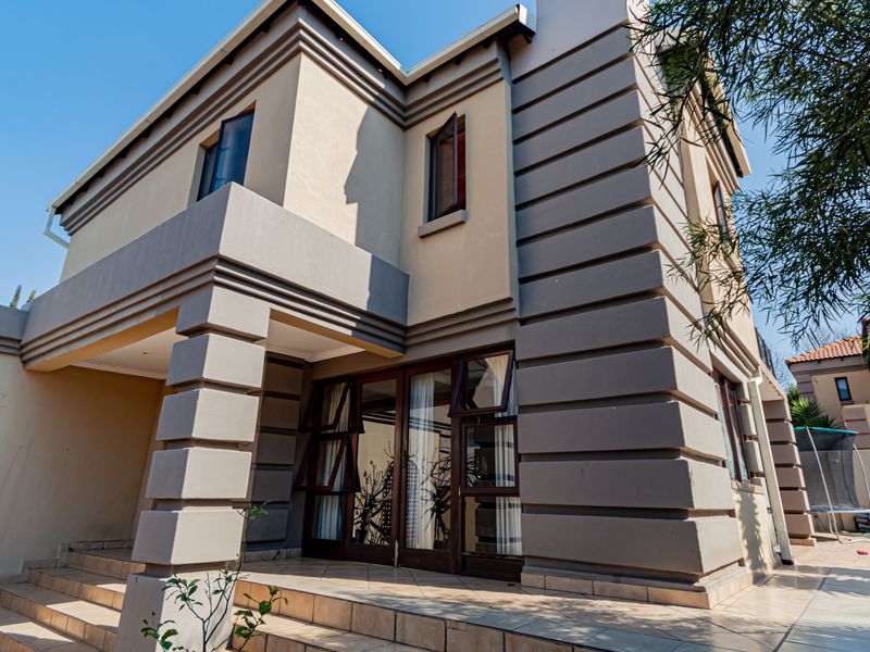 Rear view of a modern townhouse featuring a tiled patio, large sliding glass doors, and a multi-level stucco facade with architectural detailing.