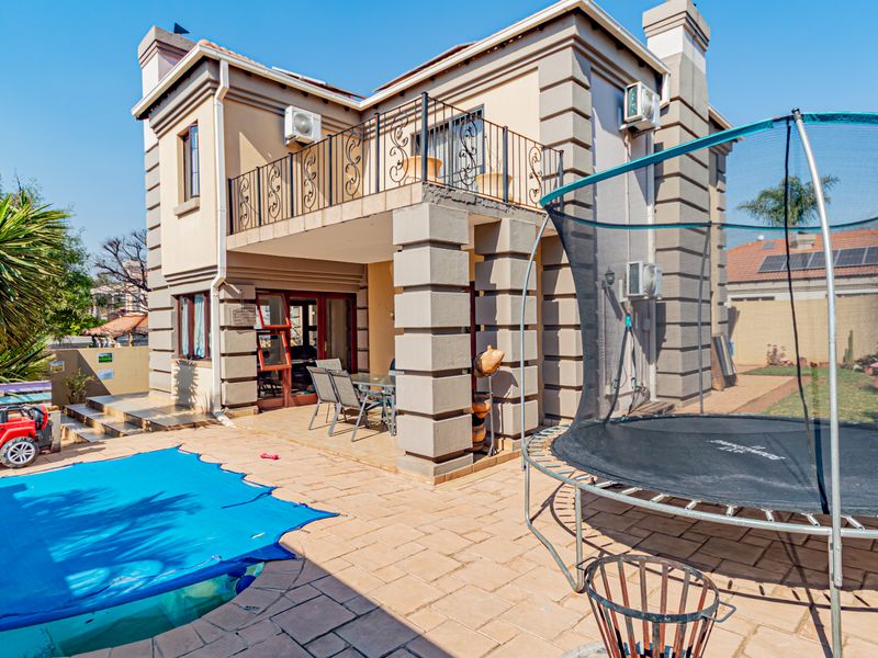 Rear view of the townhouse featuring a paved patio area, swimming pool, and an upper-level balcony with wrought iron railings.