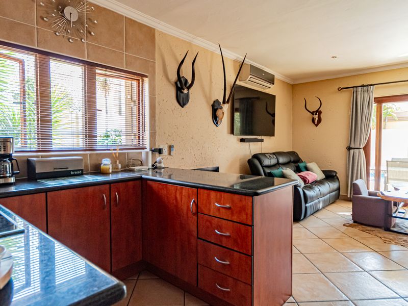 Open-plan living area featuring a kitchen with granite countertops and tiled flooring, seamlessly flowing into a lounge space with access to an outdoor patio.