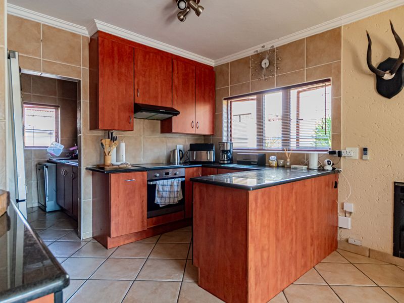 A functional kitchen featuring cherry-wood cabinetry, granite countertops, integrated appliances, and a built-in fireplace, with an adjacent scullery area.
