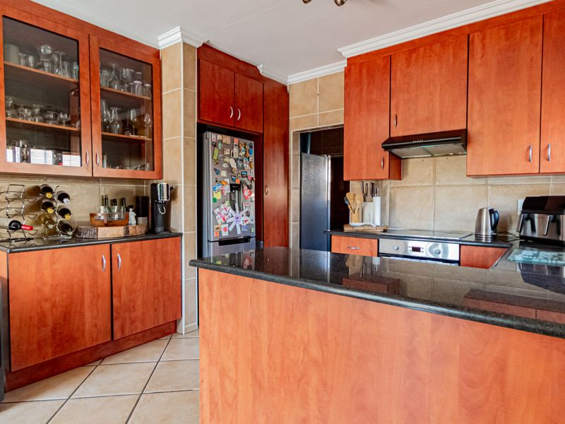 A functional kitchen featuring warm-toned wooden cabinetry, granite countertops, ceramic tiling, and integrated appliances, offering a classic and practical layout.