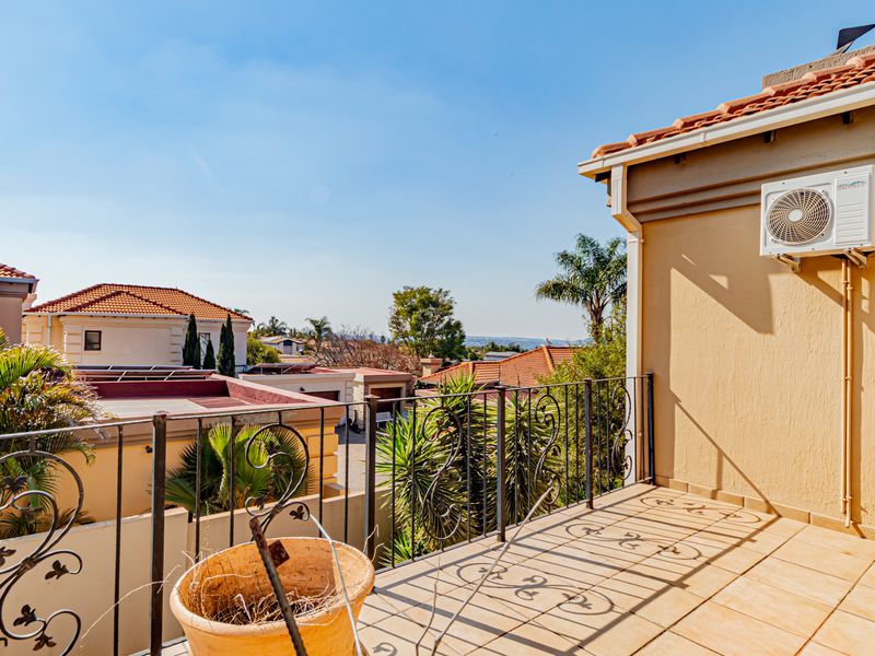 A spacious balcony featuring tiled flooring, a wrought iron railing, and a wall-mounted air conditioning unit, offering elevated views of the surrounding residential area.