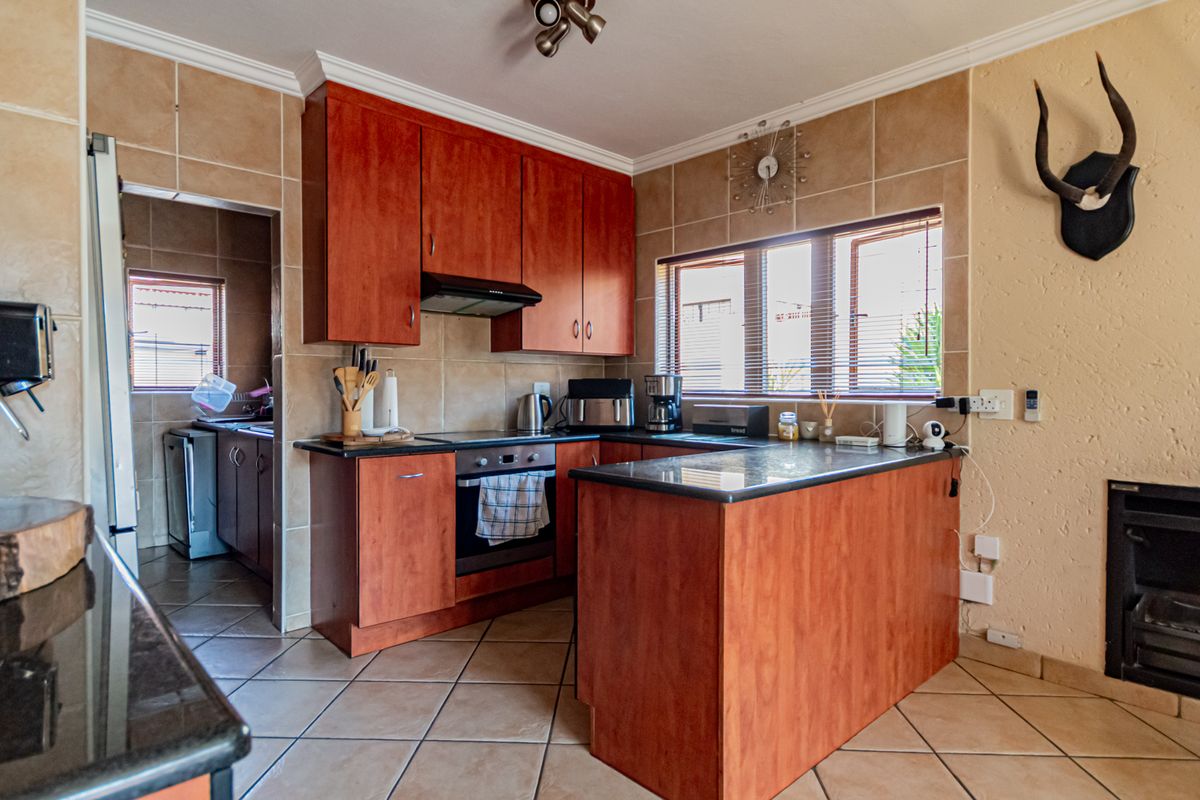 A functional kitchen featuring cherry-wood cabinetry, granite countertops, integrated appliances, and a built-in fireplace, with an adjacent scullery area.