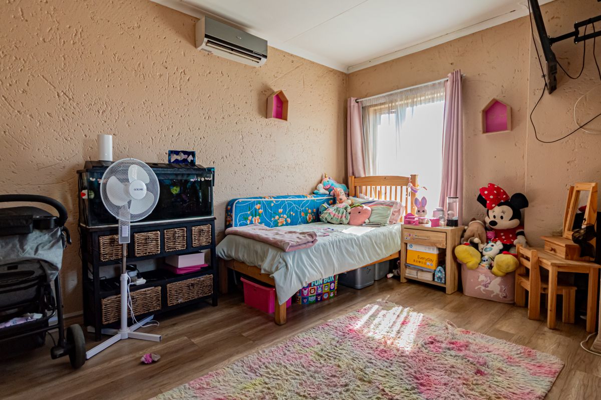 A bedroom featuring laminate flooring and a wall-mounted split-system air conditioner, providing a functional space with natural light.