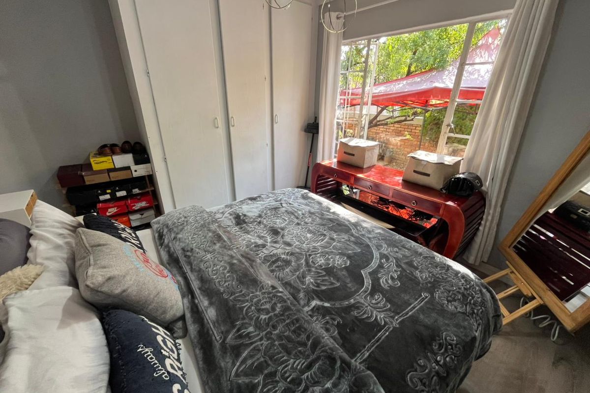 A bedroom featuring built-in cupboards and a large window providing natural light and a view of the garden area.