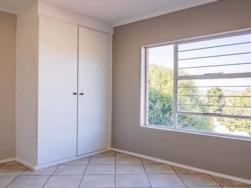 An empty bedroom featuring tiled flooring, a built-in cupboard, and a window with security bars, offering a clean and neutral space.