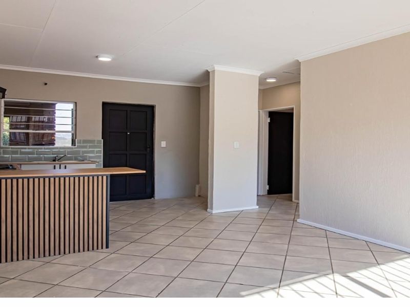 An open-plan living and kitchen area featuring tiled flooring, a modern kitchen island with wood-slat detailing, and a subway tile backsplash.