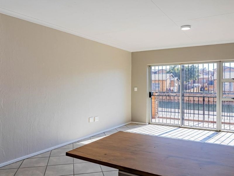 An empty living room featuring tiled floors, an exposed brick feature wall, and a sliding glass door with security gate leading to a balcony.