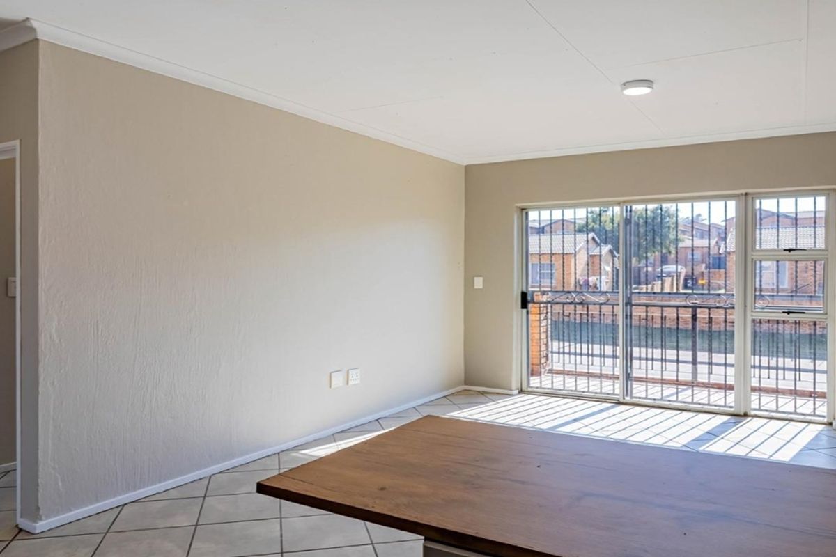 An empty living room featuring tiled floors, an exposed brick feature wall, and a sliding glass door with security gate leading to a balcony.