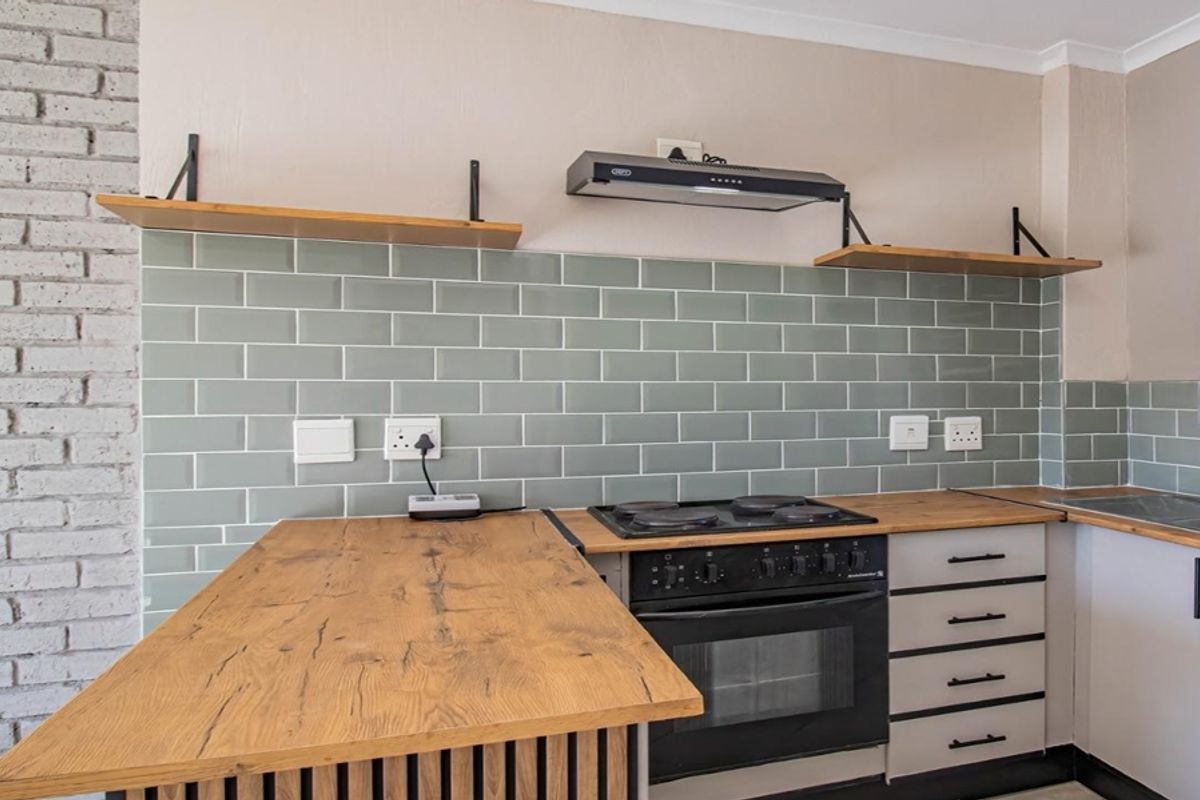 Modern kitchen featuring a stylish sage green subway tile backsplash, warm wooden countertops, built-in oven with hob, and exposed brick wall detailing.