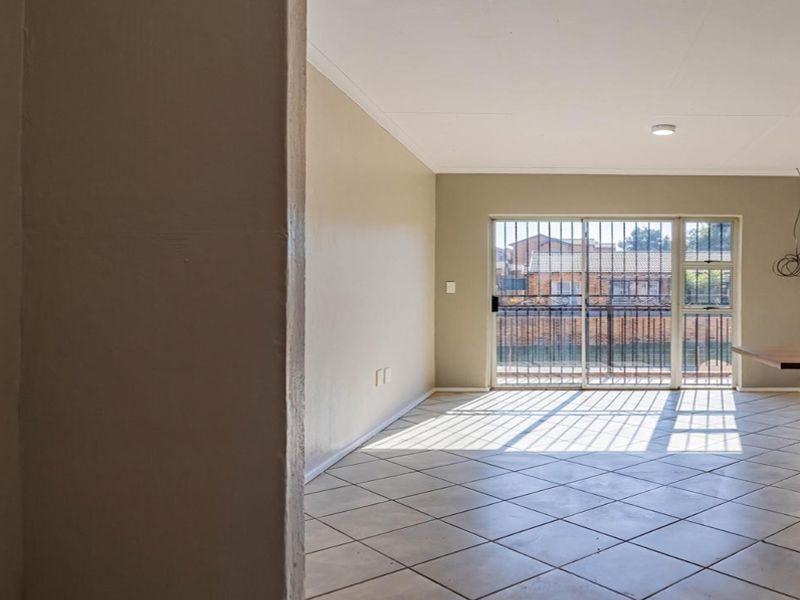 Spacious living area featuring tiled flooring, an exposed brick wall, and a sliding glass door with security bars leading to an outdoor space.