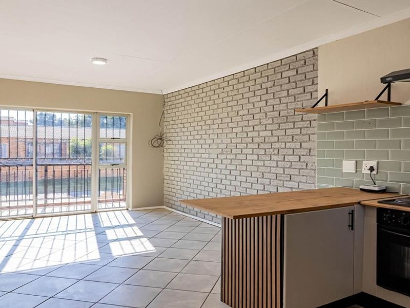 Open-plan living area featuring tiled floors, an exposed brick wall, and a modern kitchen with built-in appliances and subway tile backsplash.
