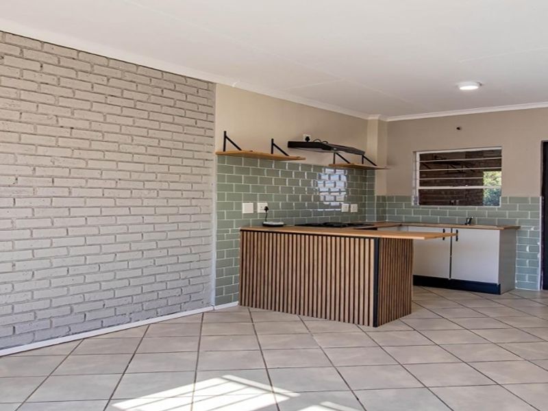 An open-plan living and kitchen area featuring tiled floors, a grey brick feature wall, and a modern kitchen island with subway tile backsplash.