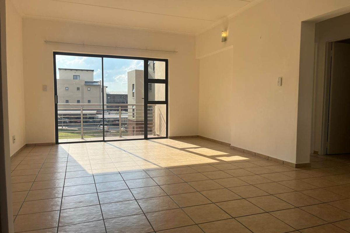 A bright, empty living room featuring neutral tiled flooring and a large sliding glass door that opens onto a balcony.