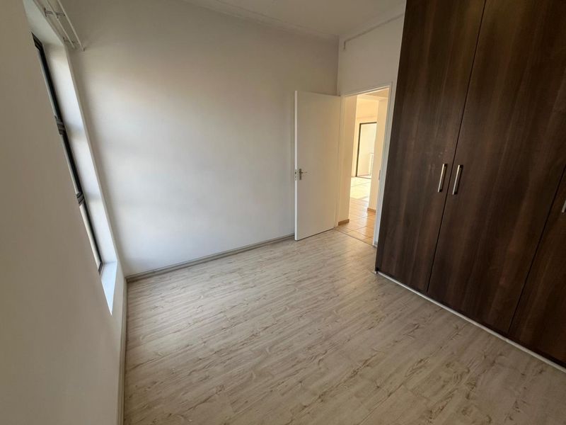 A bright, empty bedroom featuring modern laminate flooring and dark wood built-in cupboards, offering a clean and neutral space ready for personalization.