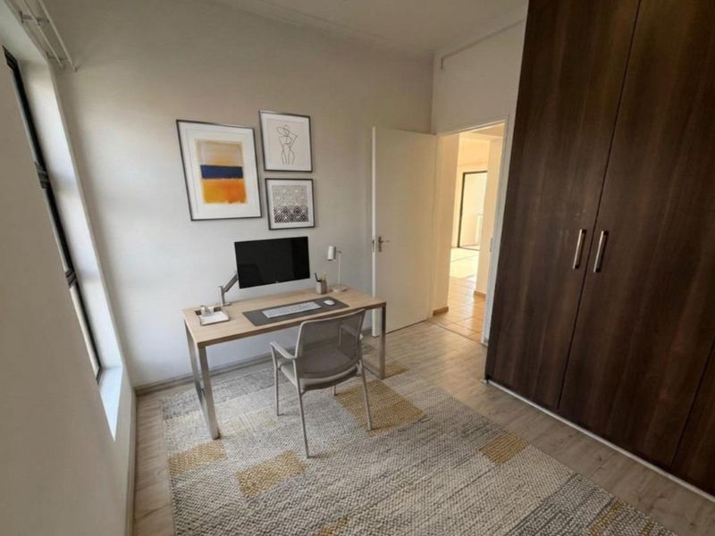 A well-lit bedroom featuring laminate flooring and a large built-in wardrobe, currently utilized as a home office space.