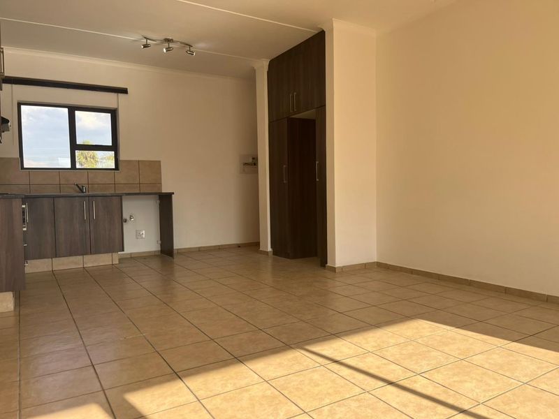 An open-plan living and kitchen area featuring tiled flooring, built-in cabinetry, and ample natural light, providing a versatile space for modern living.