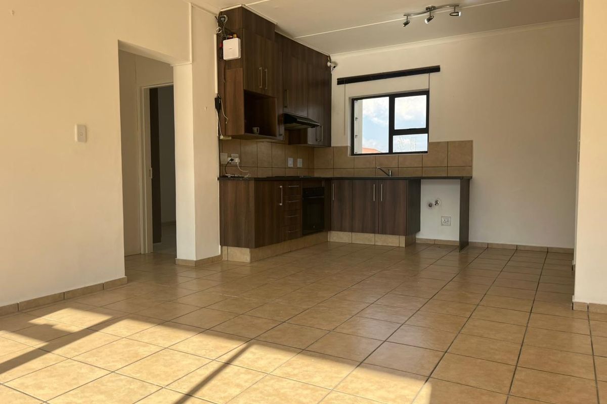 Open-plan kitchen area featuring dark wood cabinetry, tiled flooring, and built-in oven with extractor fan, offering a functional and bright living space.