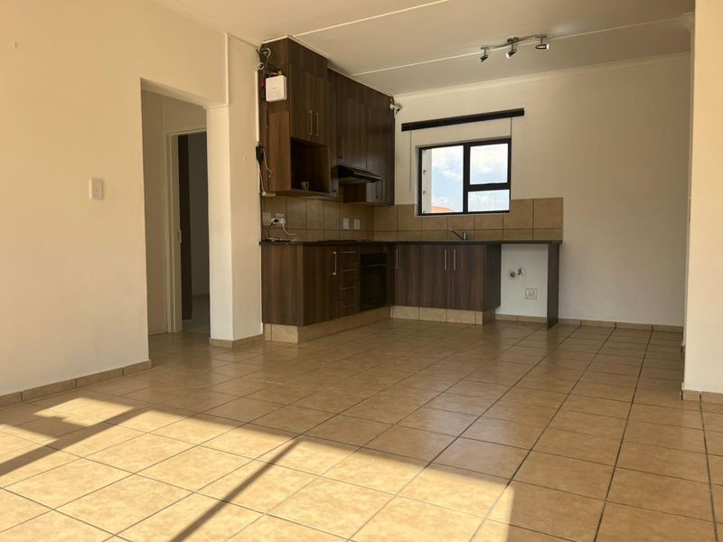 Open-plan kitchen area featuring dark wood cabinetry, tiled flooring, and built-in oven with extractor fan, offering a functional and bright living space.
