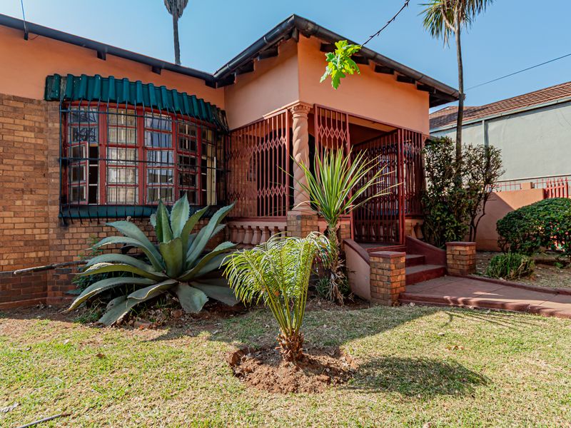 Front elevation of a brick house featuring a covered porch, security gates, and a bay window, set within a modest garden area.