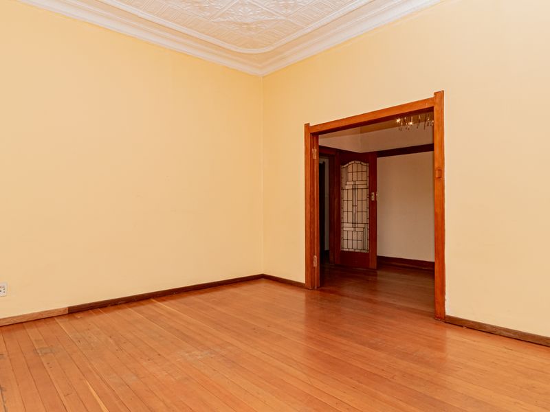 An empty living room featuring original timber flooring, ornate ceiling detailing, and a classic leaded glass door leading to an adjacent space.