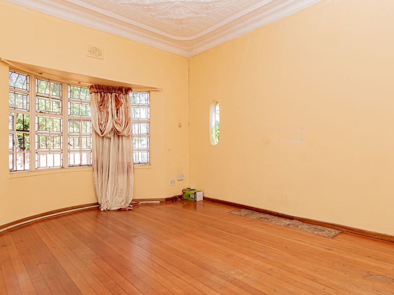 Spacious living room featuring original hardwood flooring, a decorative pressed metal ceiling, and charming stained glass windows.
