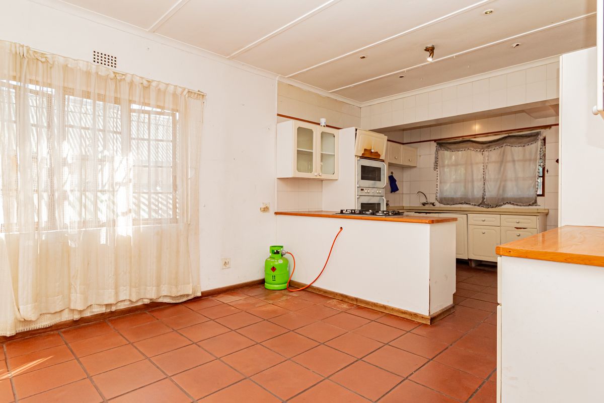 A dated kitchen featuring tiled flooring, built-in cabinetry, a gas hob, and an integrated oven, offering potential for a modern renovation.