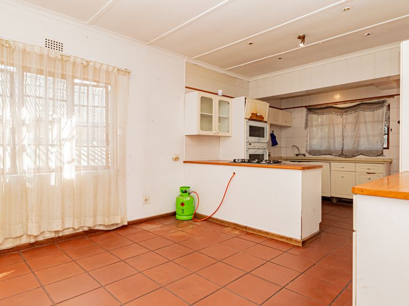 A dated kitchen featuring tiled flooring, built-in cabinetry, a gas hob, and an integrated oven, offering potential for a modern renovation.