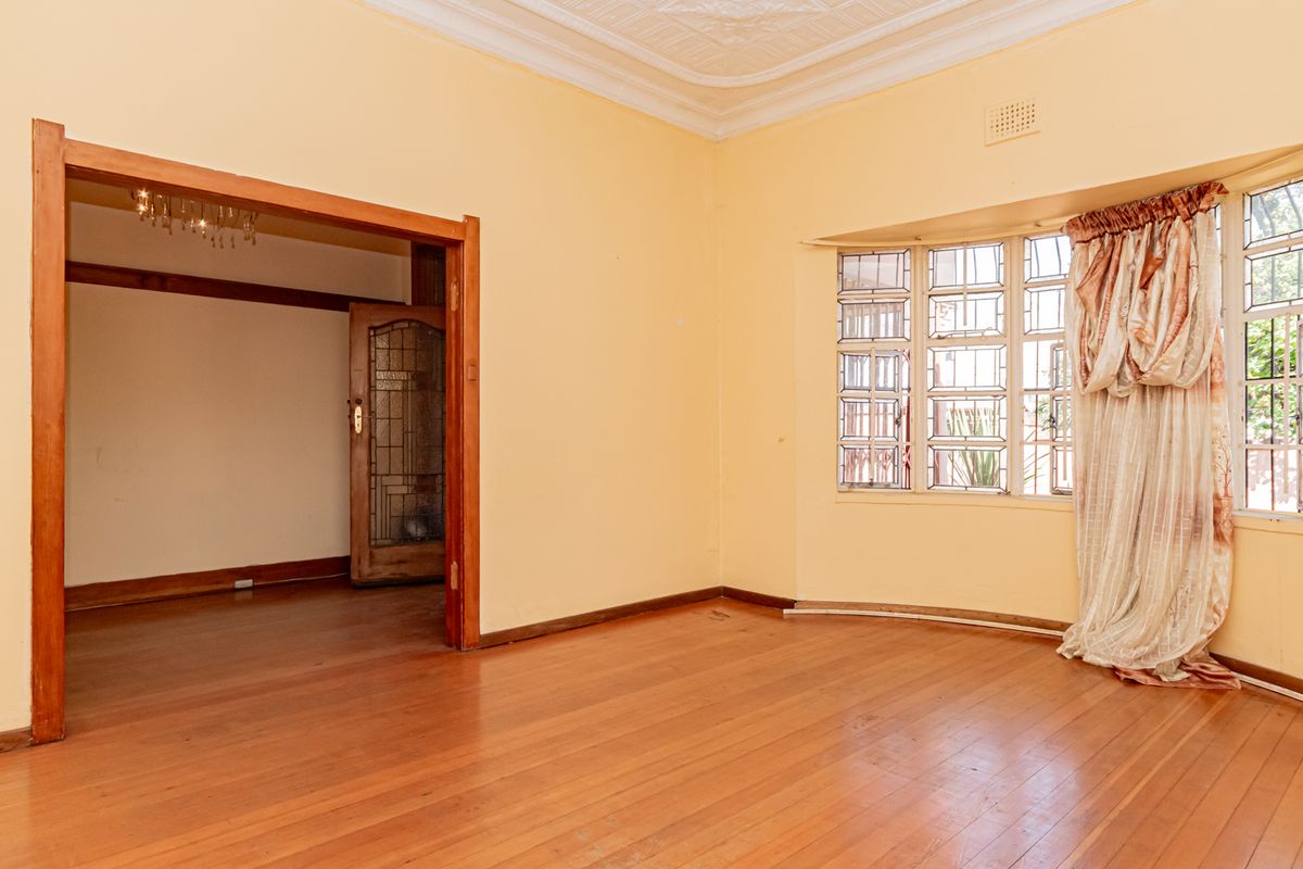 Spacious living room featuring original hardwood flooring, ornate ceiling detailing, and a classic bay window with leaded glass accents.