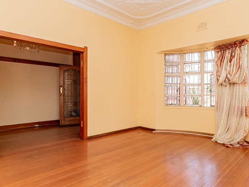 Spacious living room featuring original hardwood flooring, ornate ceiling detailing, and a classic bay window with leaded glass accents.