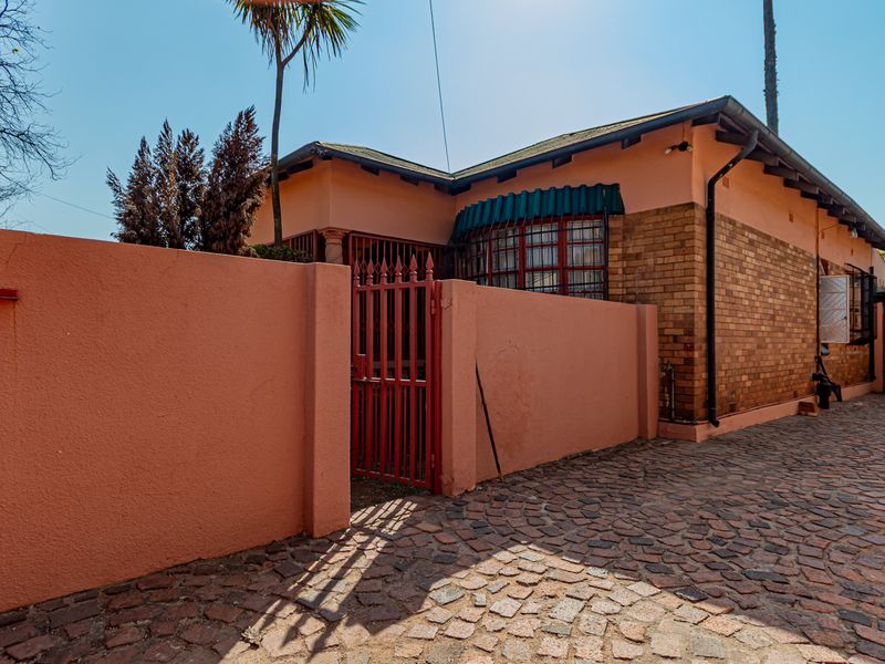 Front exterior view of a single-story house featuring a brick facade, a gated entrance, and a cobblestone driveway leading to a carport.