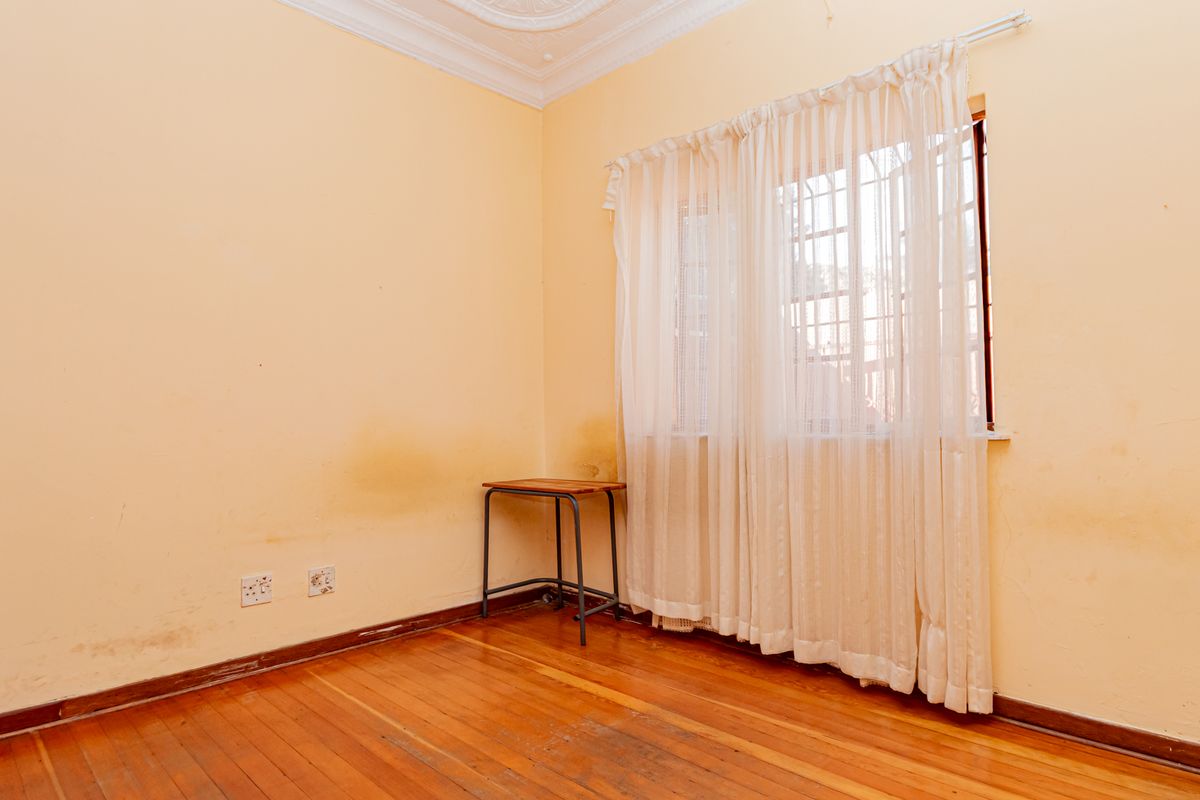 An empty bedroom featuring original hardwood flooring, ornate ceiling cornicing, and a window fitted with security bars.