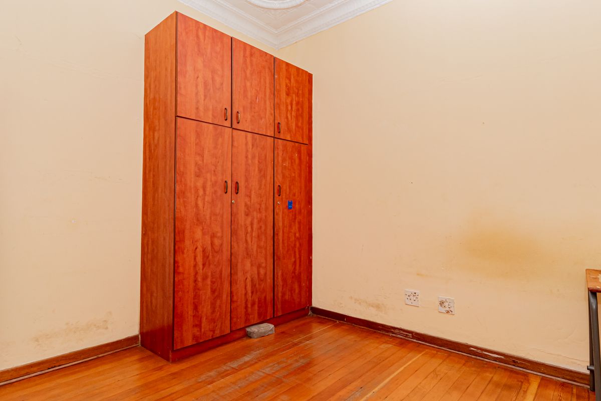 A vacant bedroom featuring hardwood flooring, a built-in wooden wardrobe, and decorative ceiling cornice, requiring cosmetic updates to the walls and flooring.
