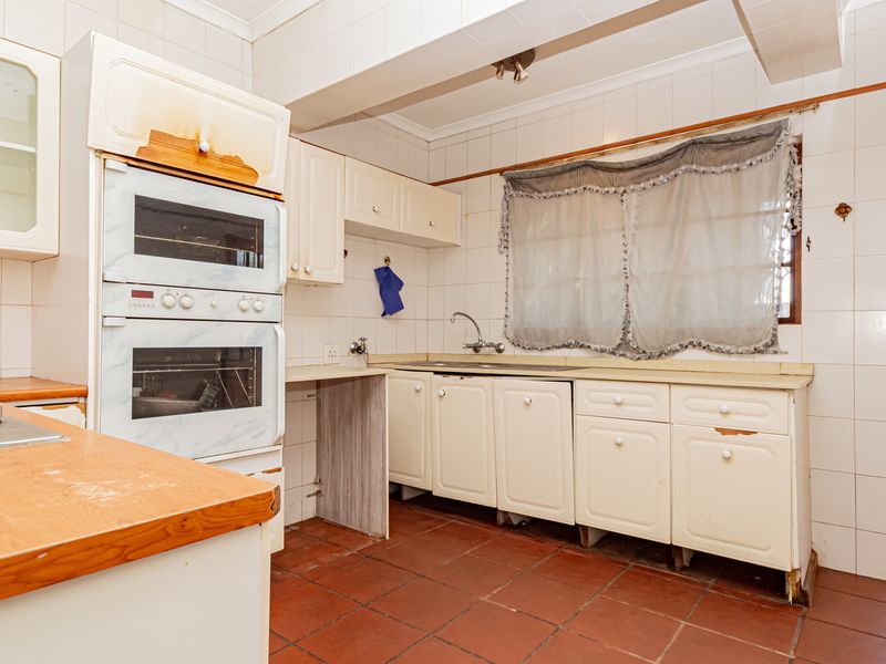 A dated kitchen featuring built-in double ovens, a gas hob, tiled walls, and terracotta flooring, offering significant potential for modernization and renovation.