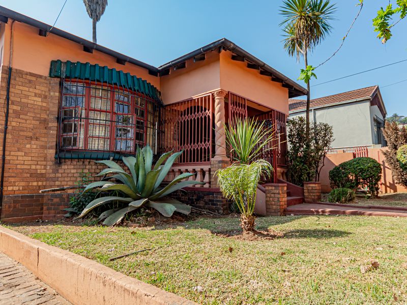 Front view of a traditional brick house featuring a covered porch, security gates, and a landscaped front garden area.