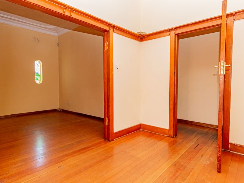 An empty hallway featuring original timber flooring, classic timber door frames, and a decorative stained glass window, offering a traditional architectural aesthetic.