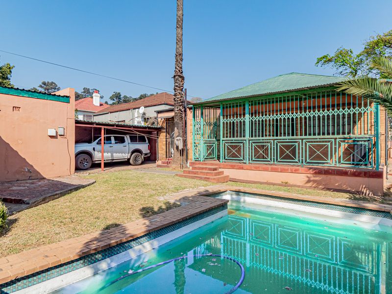 Rear exterior view featuring a swimming pool, paved surround, covered patio with security gates, and a carport area.