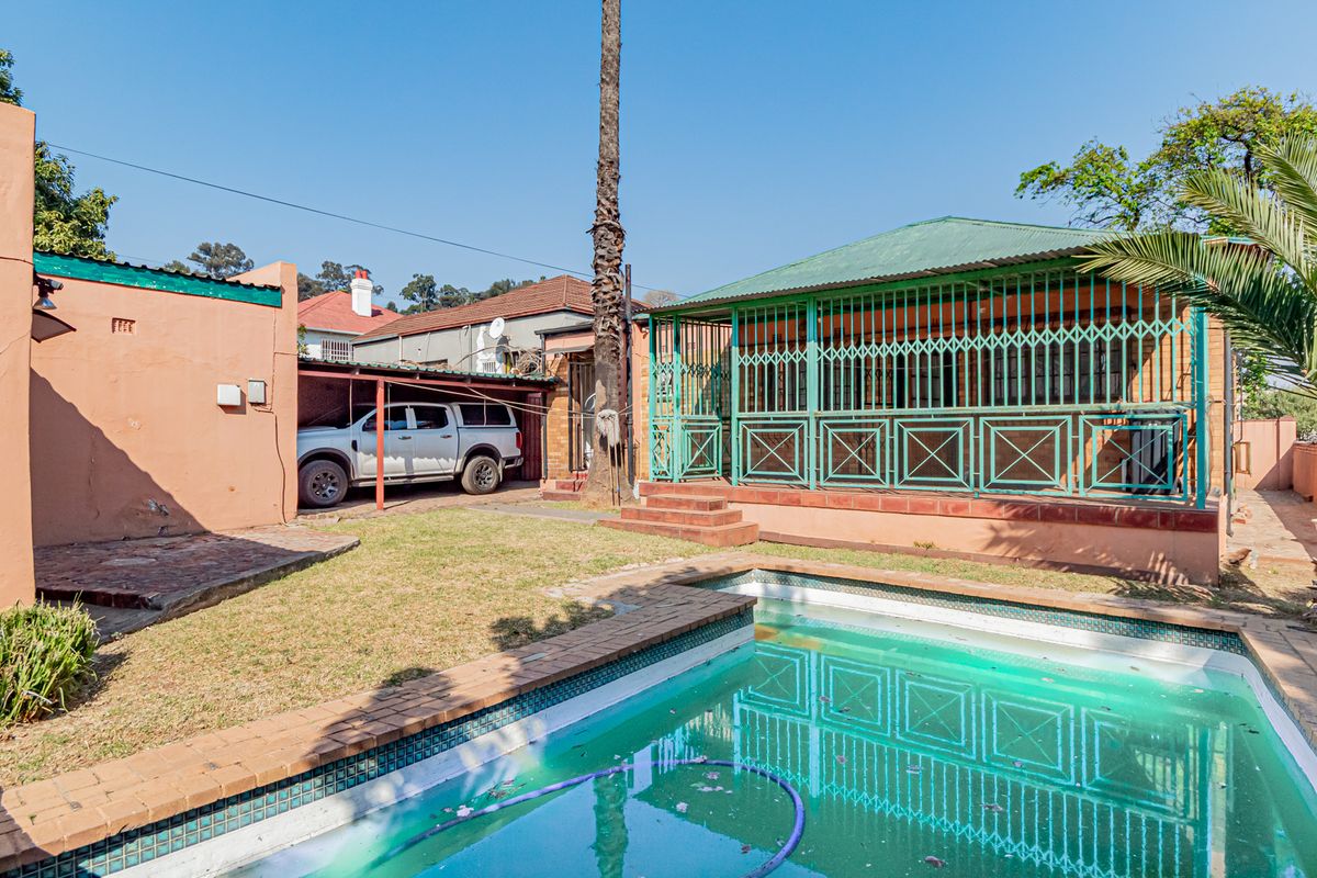 Rear exterior view featuring a swimming pool, paved surround, covered patio with security gates, and a carport area.