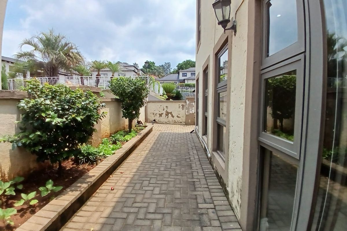 A side exterior walkway featuring paved flooring, a retaining wall, and aluminium window frames, showing signs of wear on the exterior wall finish.