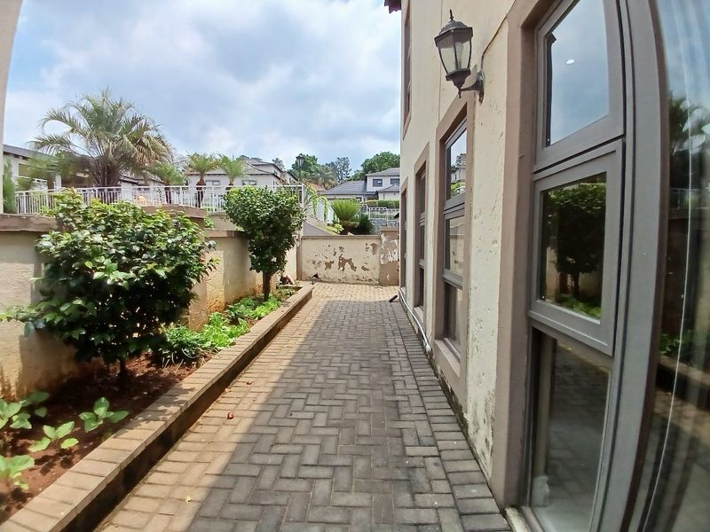 A side exterior walkway featuring paved flooring, a retaining wall, and aluminium window frames, showing signs of wear on the exterior wall finish.