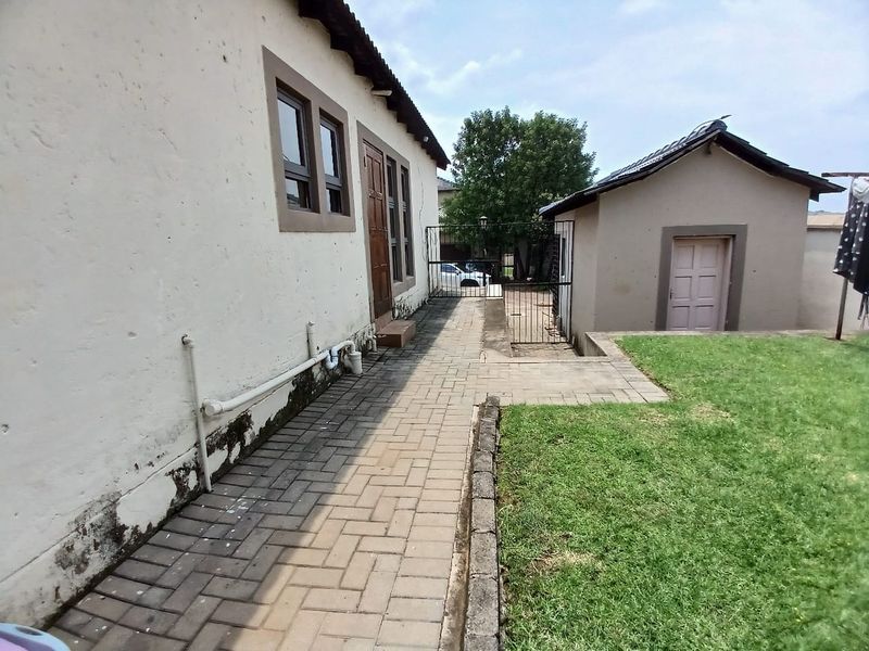 Rear exterior view of the townhouse featuring a paved walkway, small lawn area, and a detached outbuilding with security gate access.