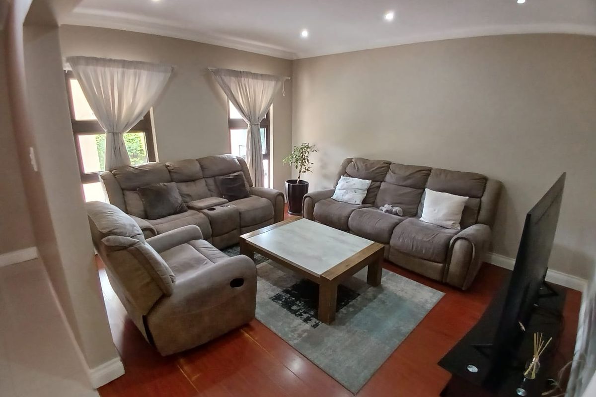 A comfortable living room featuring warm laminate flooring, recessed downlighting, and coved ceilings, creating a welcoming and well-maintained space.