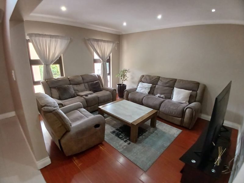 A comfortable living room featuring warm laminate flooring, recessed downlighting, and coved ceilings, creating a welcoming and well-maintained space.