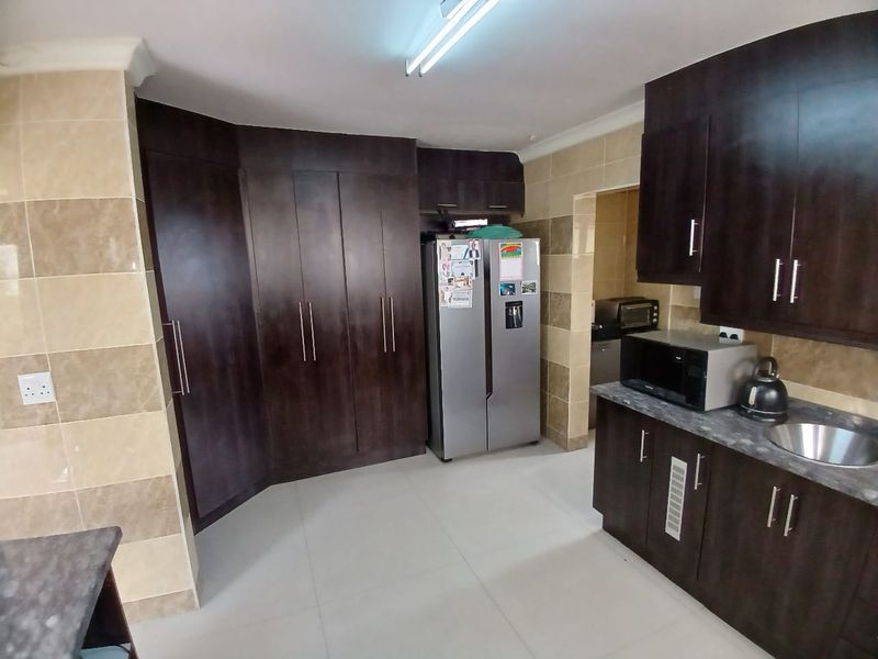 A functional kitchen featuring dark wood cabinetry, tiled walls, and ample storage space with a neutral tiled floor.