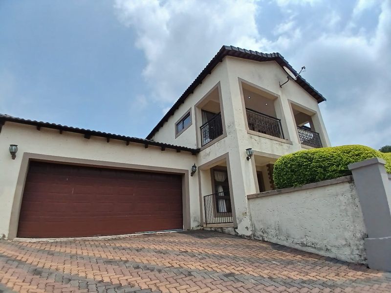 Front elevation of a double-story townhouse featuring a double garage, paved driveway, and upper-level balcony with wrought iron railings.